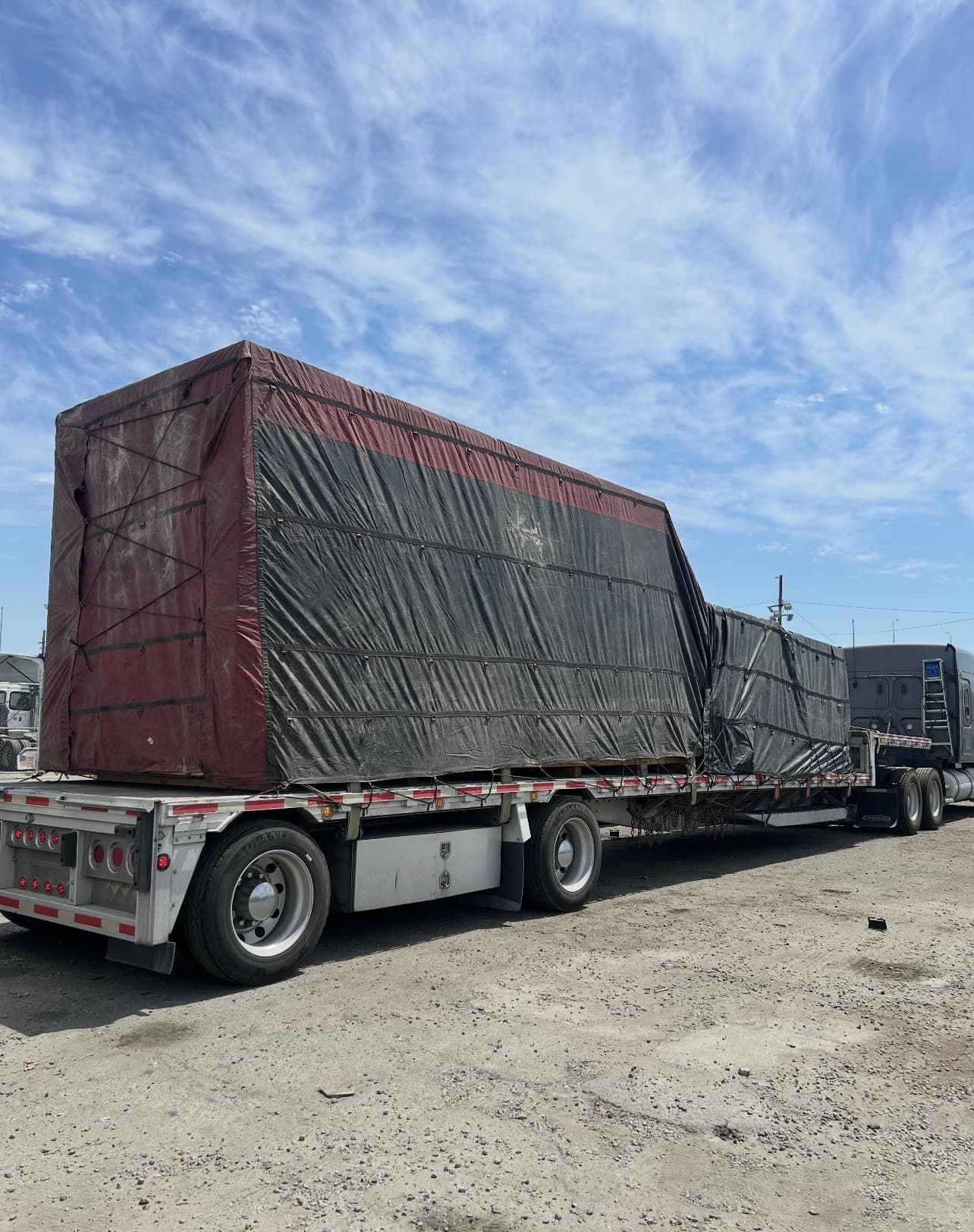 Covered general freight secured on a flatbed trailer for transportation.